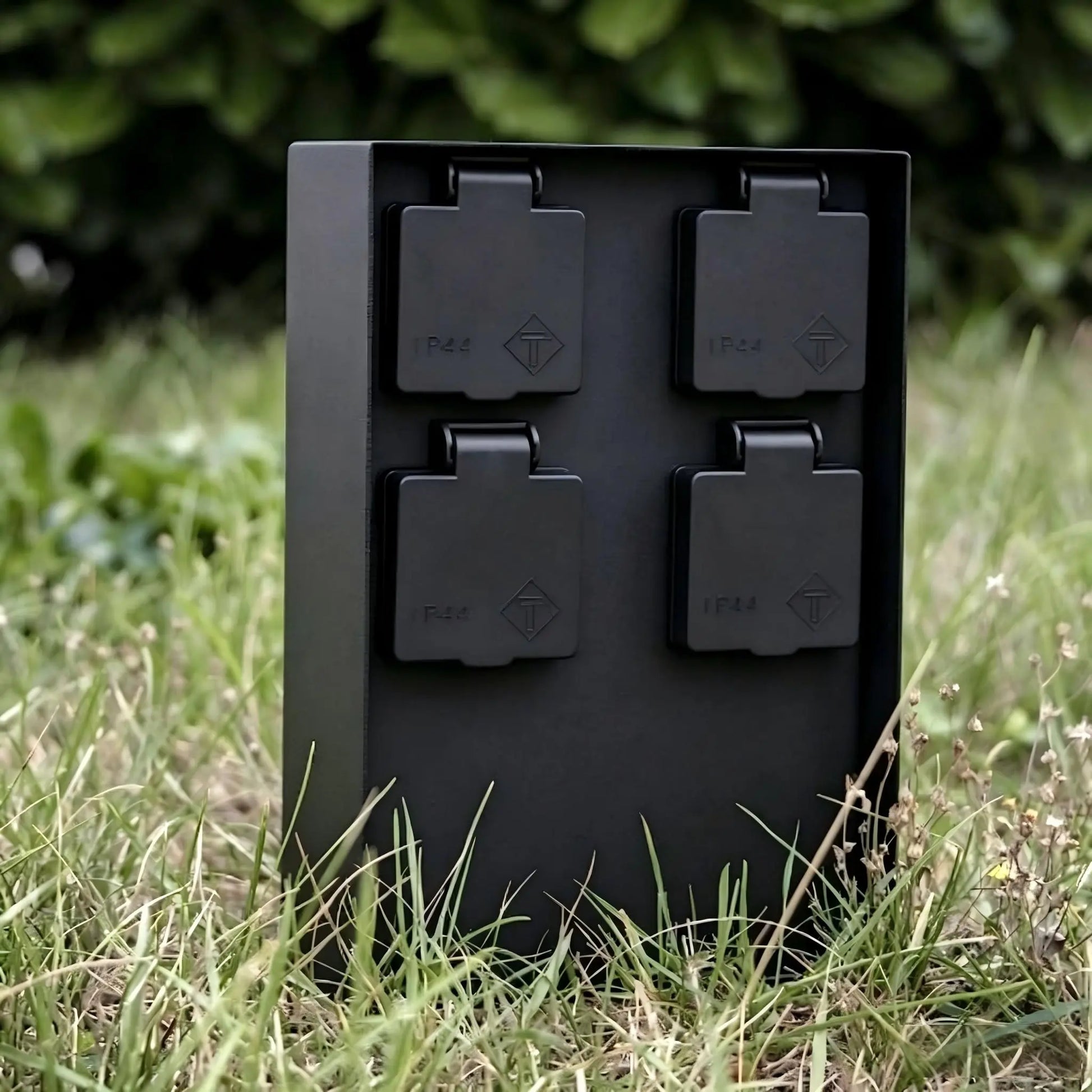 Close-up of a black IP44 weatherproof 4-outlet garden power column surrounded by green grass