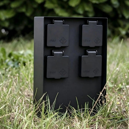 Close-up of a black IP44 weatherproof 4-outlet garden power column surrounded by green grass