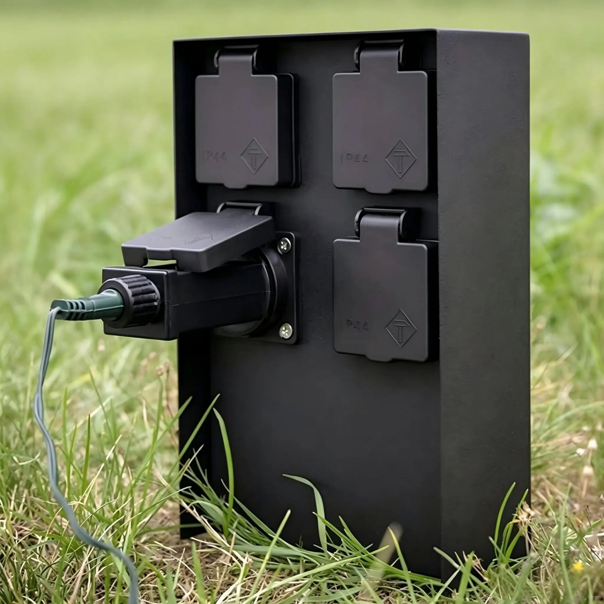 Black outdoor 4-way power socket box in use with a cable plugged into one of the IP44 protected outlets