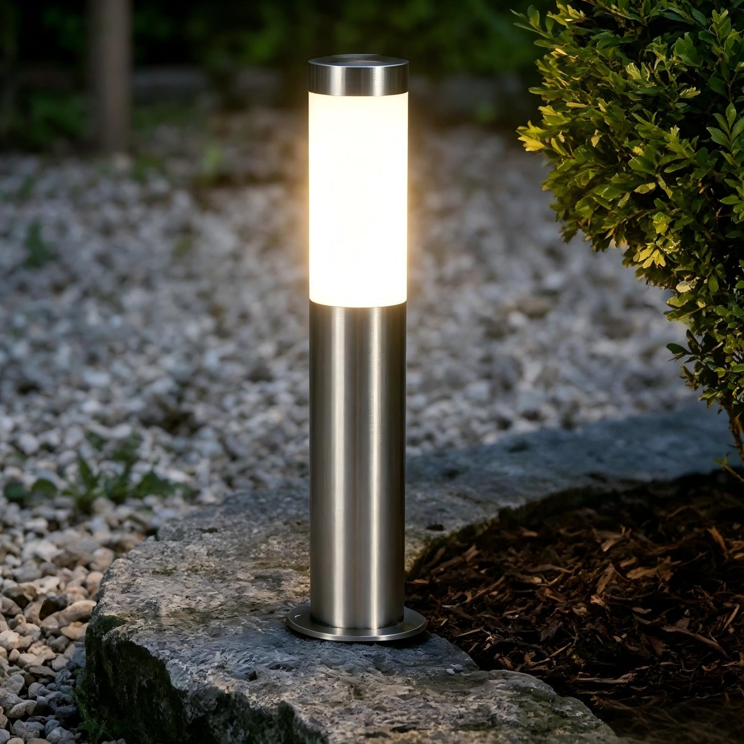 Modern stainless steel garden bollard light illuminating an outdoor pathway.